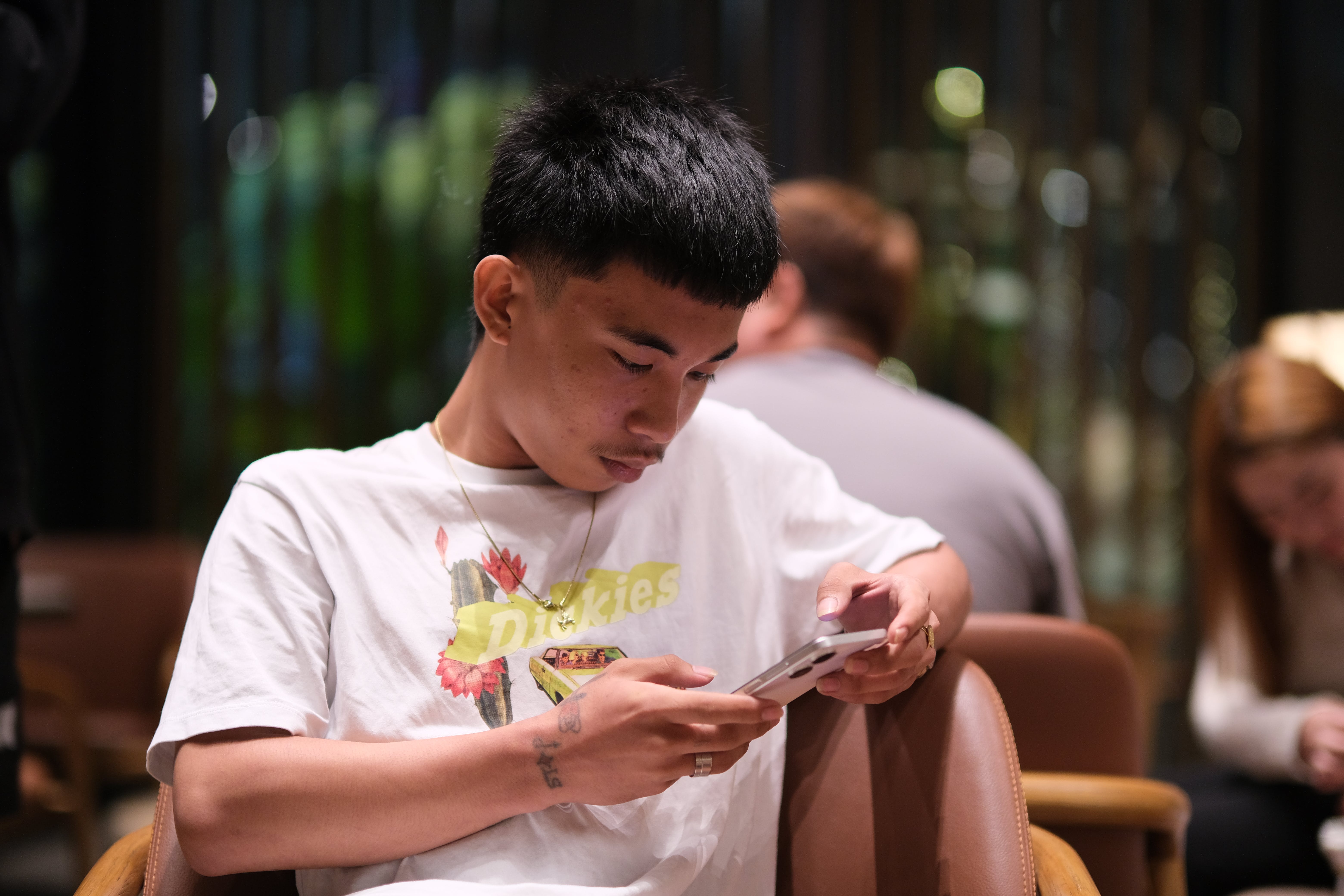 Foto van jonge man die op een stoel zit en op zijn smartphone kijkt.